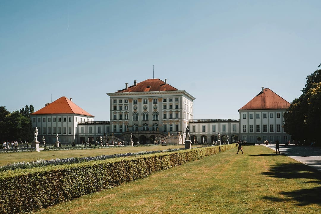 Nymphenburg Palace in Munich, Germany, with manicured gardens and visitors enjoying a sunny day.