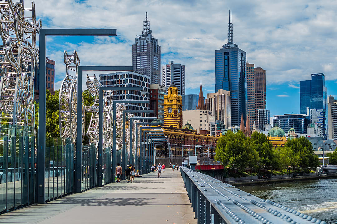 Scenic view of Melbourne’s city skyline at sunset, with modern skyscrapers reflecting in the tranquil Yarra River, framed by lush greenery along the waterfront