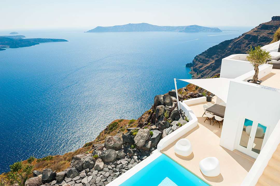 High-angle view of a luxury white villa with a private infinity pool overlooking the ocean in Santorini.