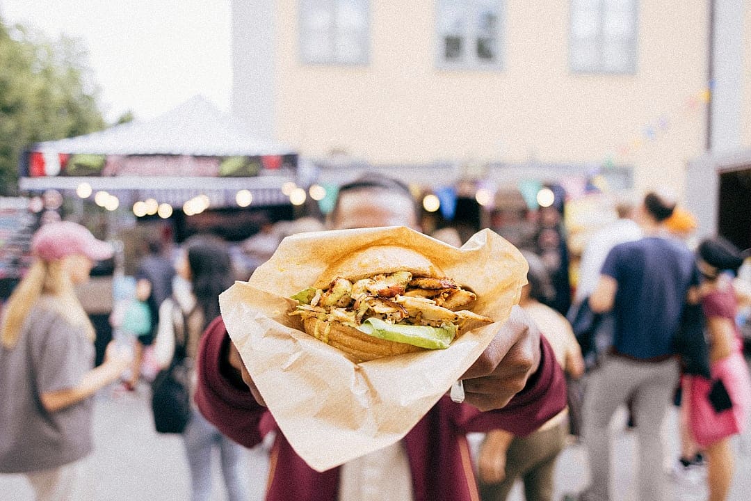 Close-up of gourmet sandwich at Taste of Stockholm, with a lively outdoor festival in the background.