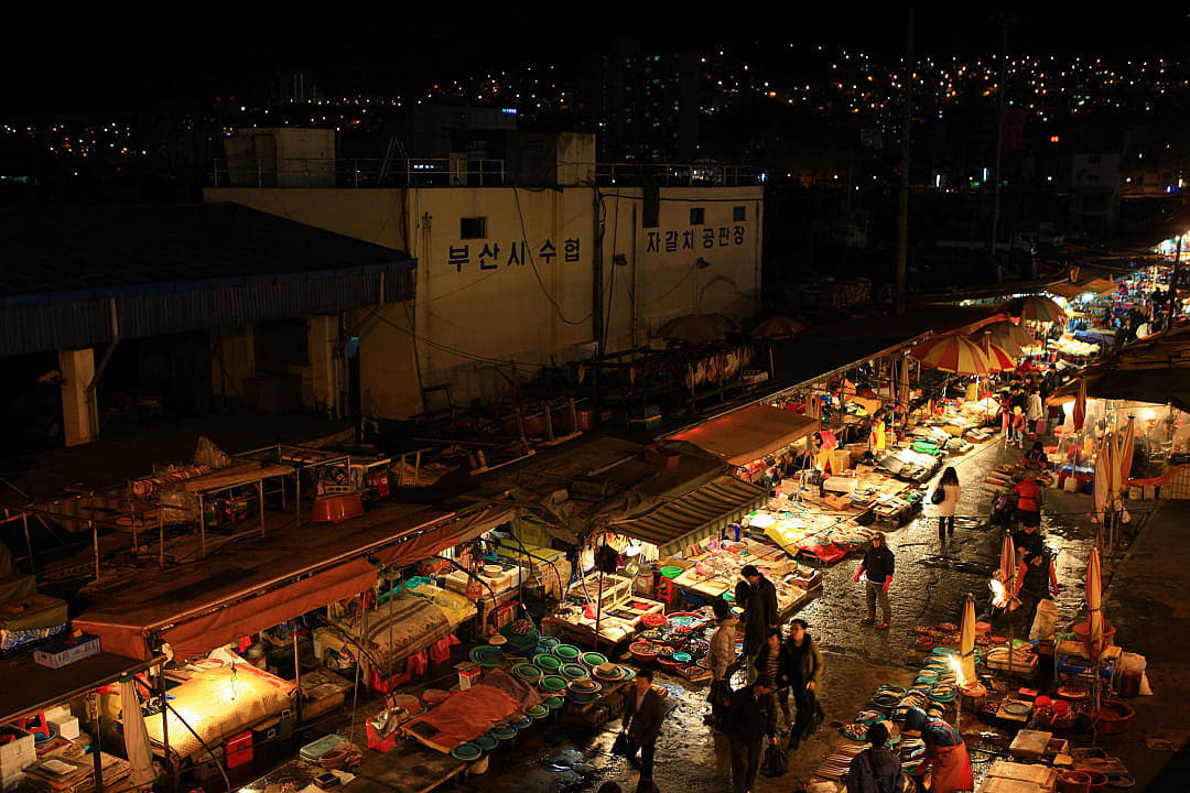 A vibrant traditional market at night with stalls lit up and people shopping.