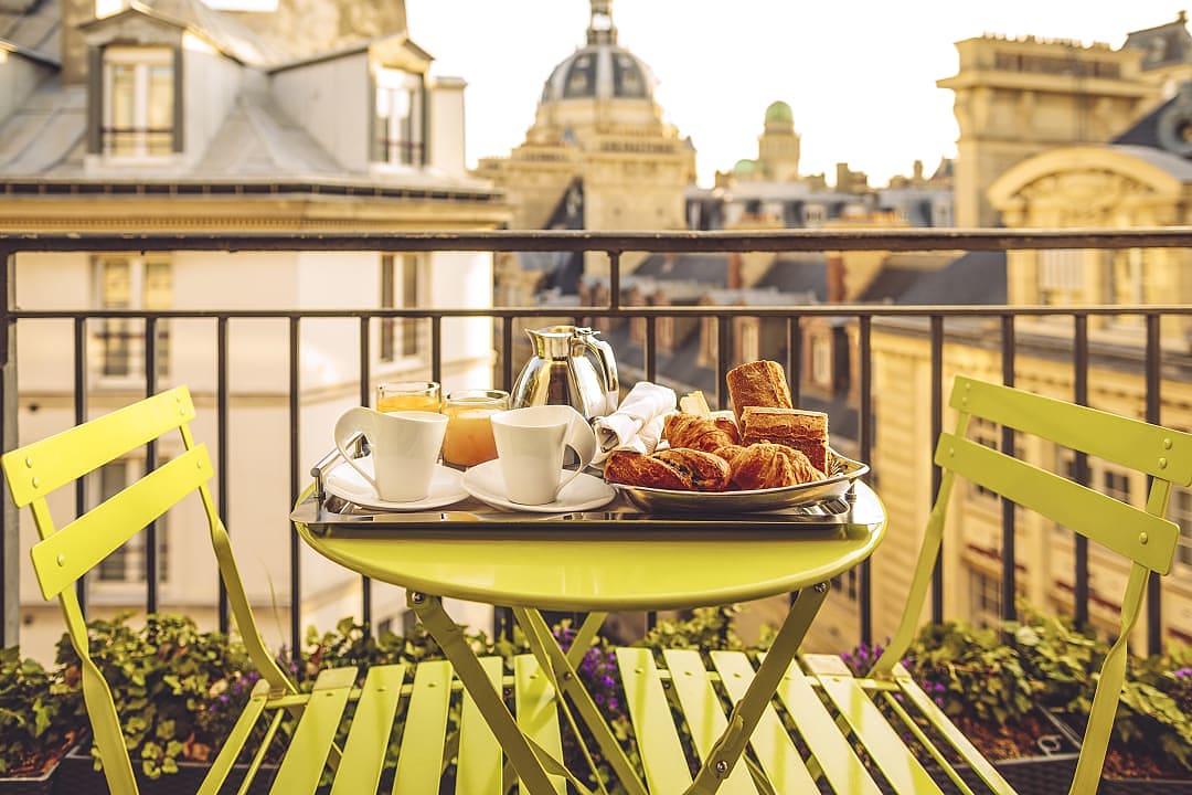 Elegant Parisian hotel breakfast with fresh pastries and coffee, enjoyed on a private balcony with stunning city views.