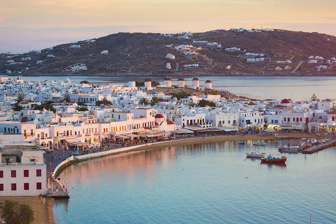Colorful waterfront and windmills at sunset in Mykonos, Greece.