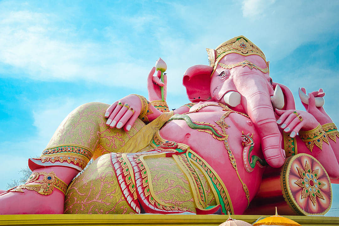 Massive pink Ganesha statue reclines under blue sky in Thailand.