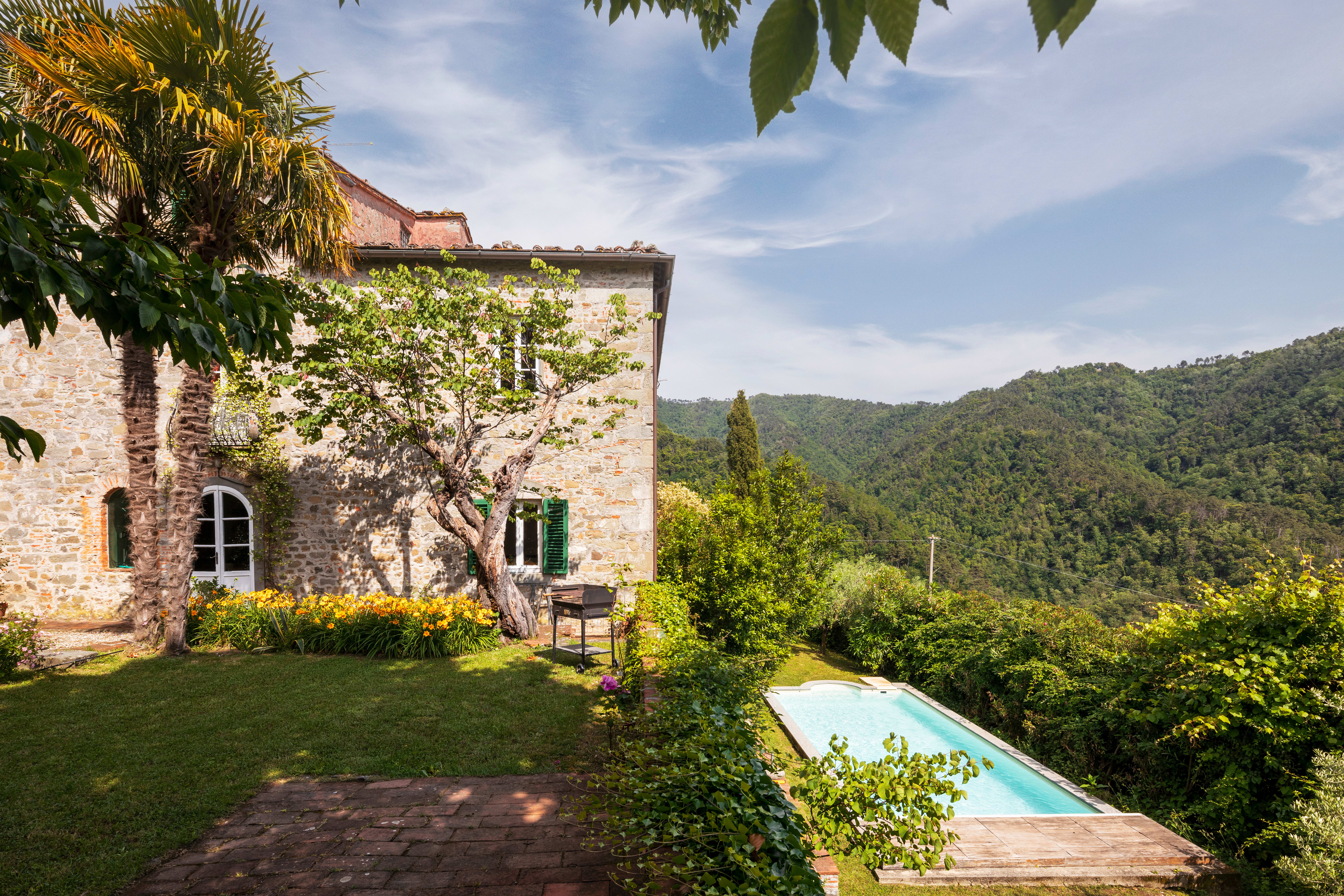 A rustic stone villa with a private garden and a small swimming pool overlooking a lush mountain valley.