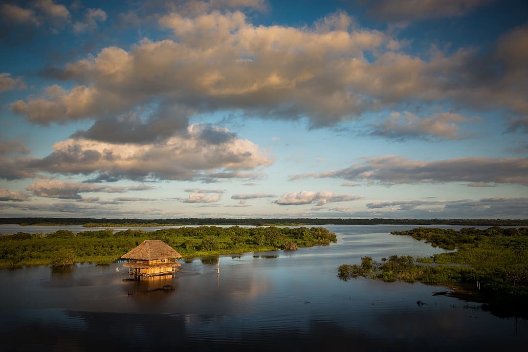 Scenic view of a rustic floating lodge surrounded by lush greenery on the Amazon River at sunset