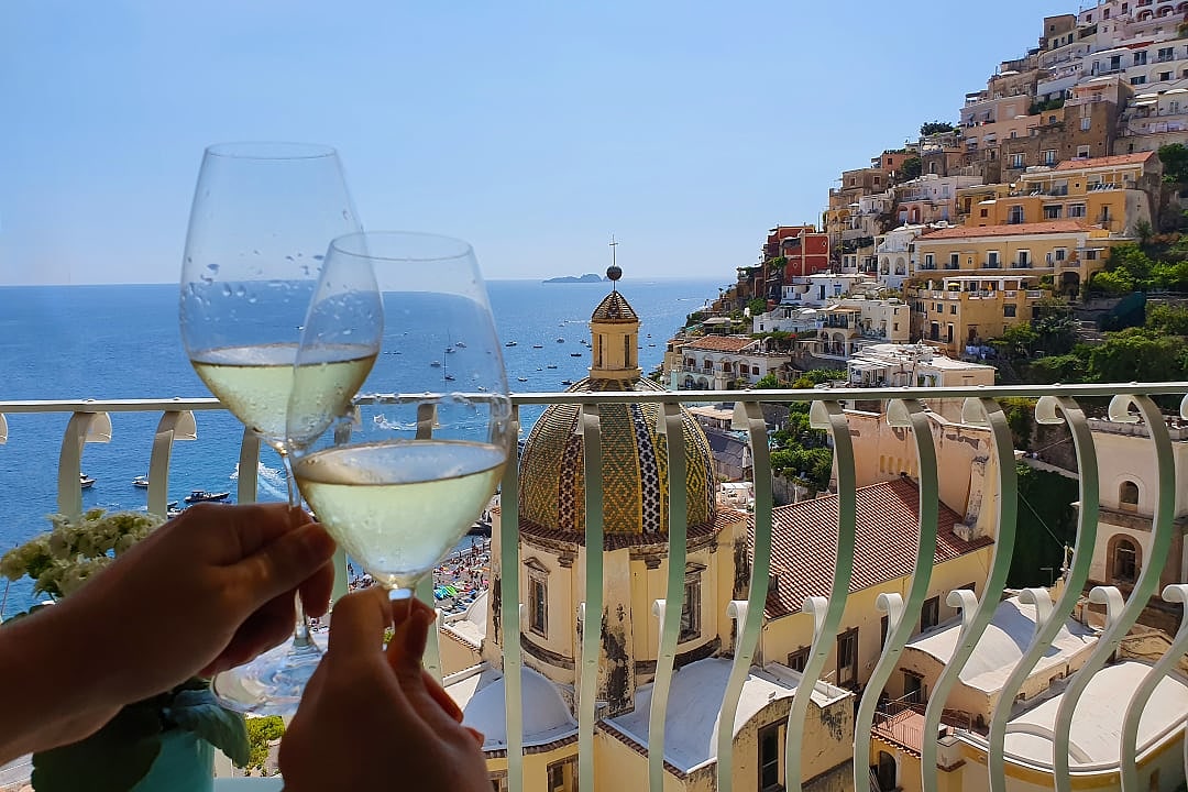 Couple holding wine glasses with Positano view on the Amalfi Coast