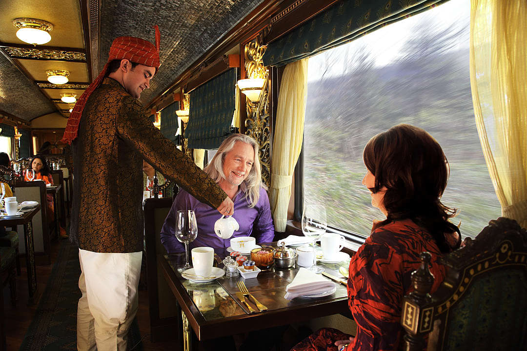 Elegant train dining with waiter serving tea to smiling guests.