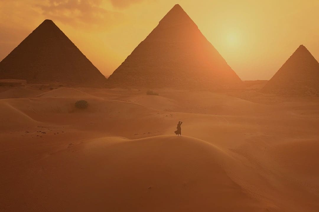 Woman on a sand dune looking a the Pyramids of Giza in Egypt