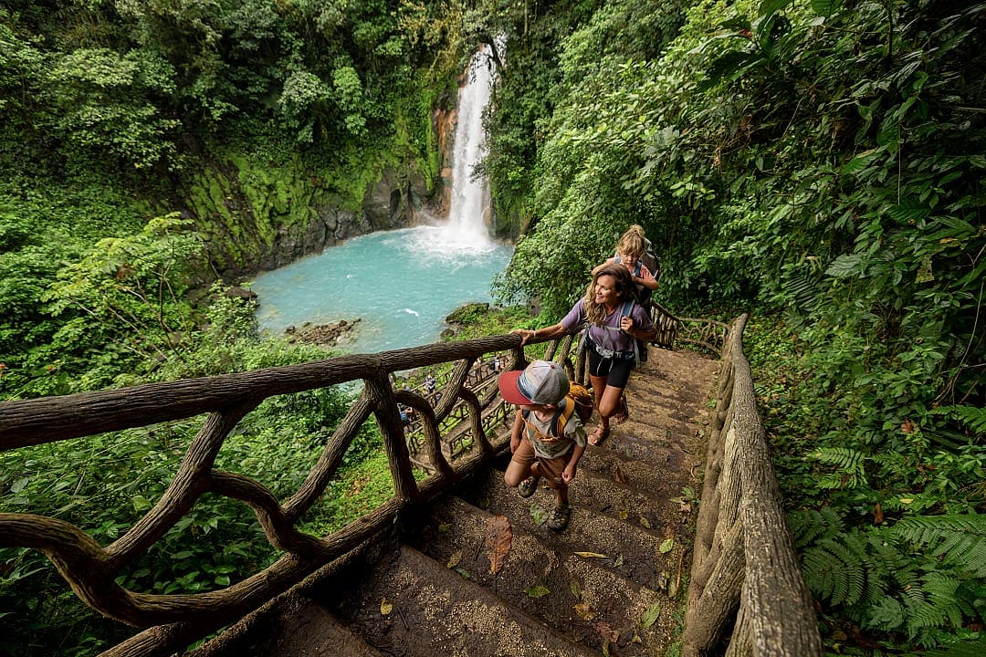 Family hiking down a wooden staircase to Rio Celeste waterfall in Tenorio Volcano National Park, Costa Rica