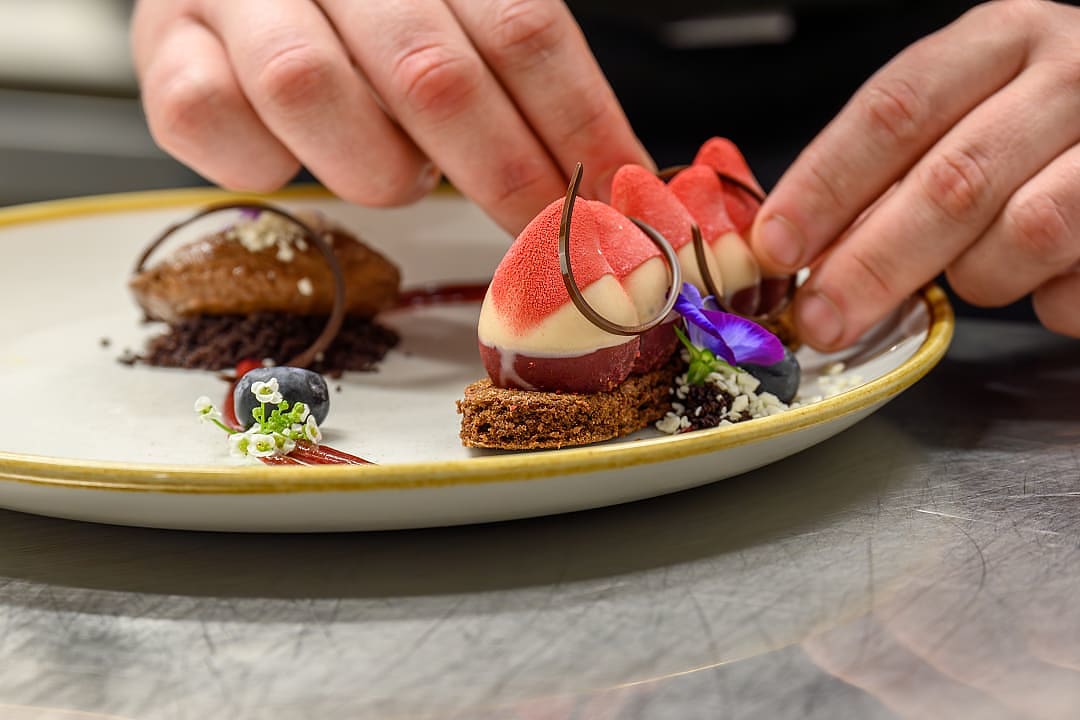 A chef delicately plating an elegant trio of modern desserts, Australia.