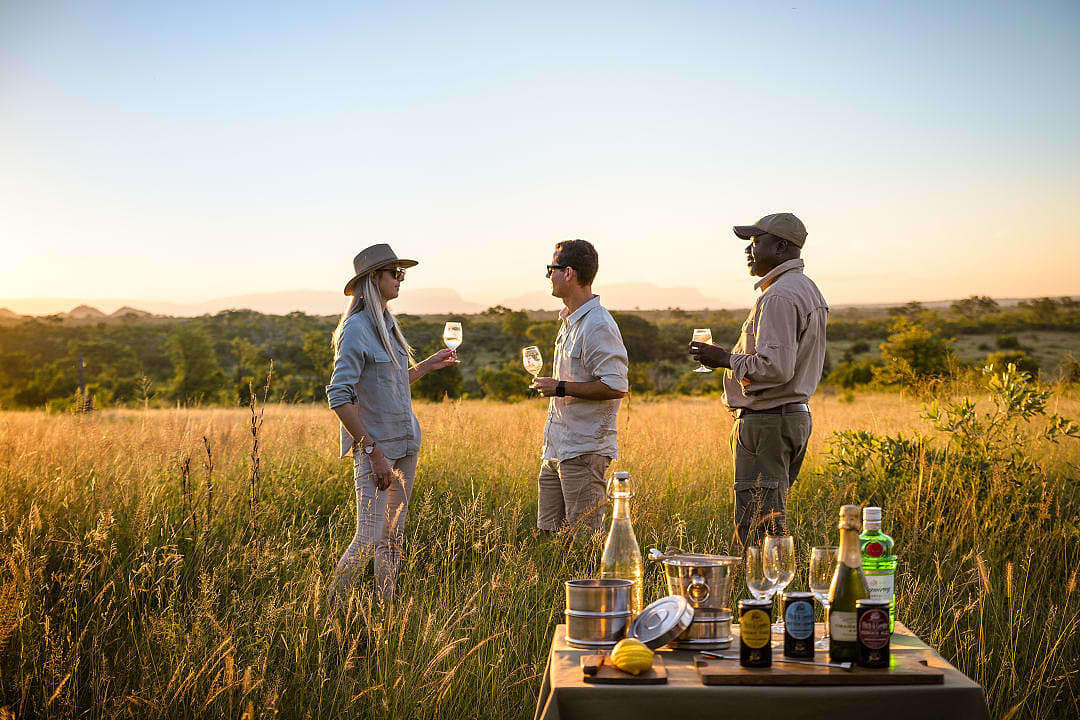 Travelers enjoying sundowners in the African bush with drinks at golden hour