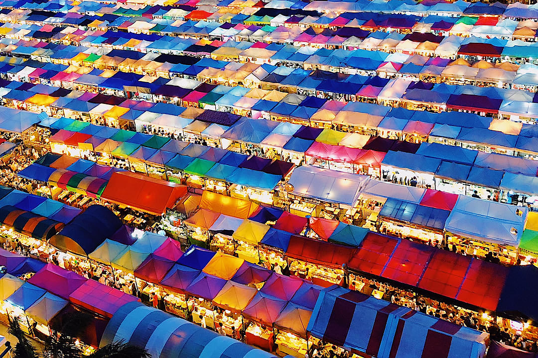 Colorful market tents glow at night in bustling Bangkok street market.