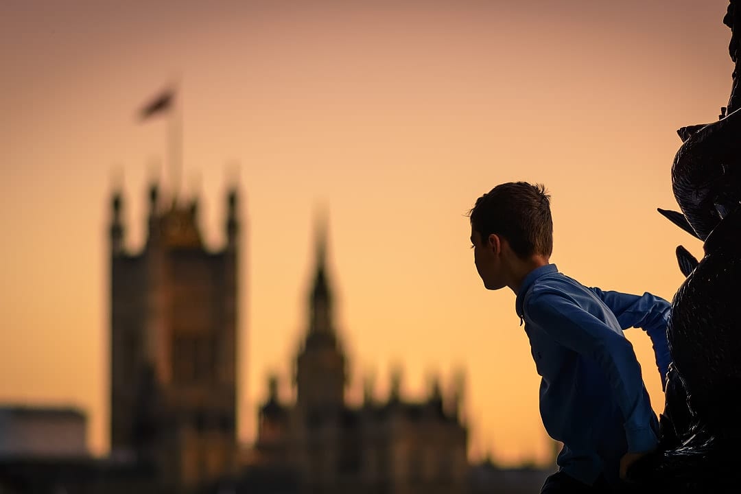 Child climbing a lamp post in london at sunset with the houses of parliament in the background