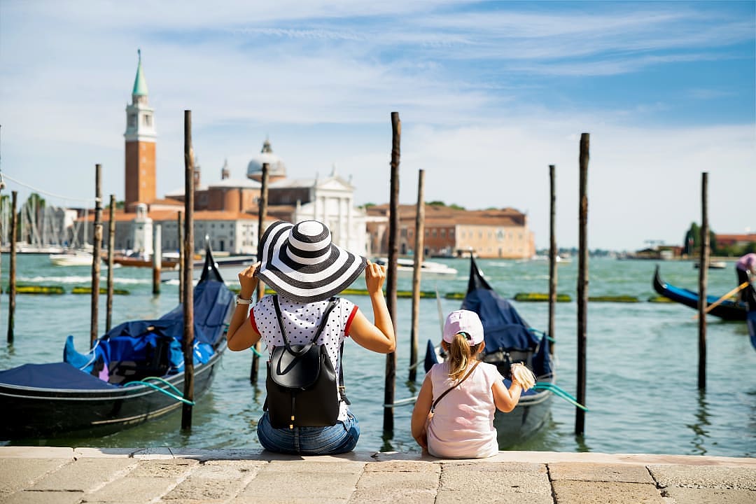 Mother and daughter sitting in front of gondolas looking at San Giorgio Maggiore in Venice, Italy