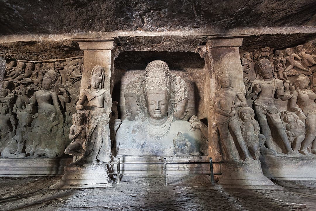 Stone trimurti sculpture inside ancient cave temple on elephanta island.
