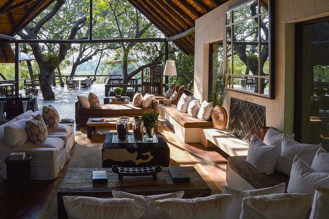 Sun-drenched open-air lounge of a luxury safari lodge, with plush white sofas and views of the surrounding bushveld