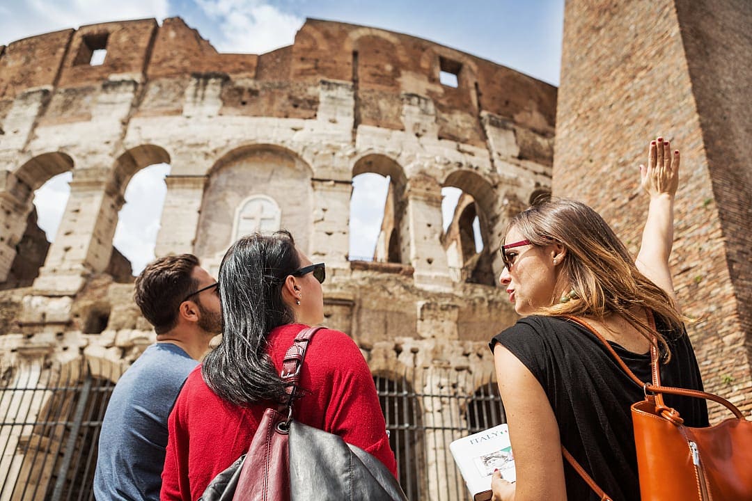 A traveler in a red shirt stands with a private guide in front of the stone arches of the Coliseum in Rome.