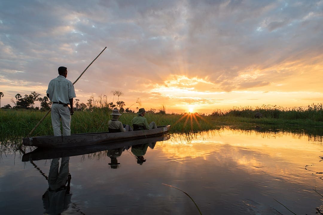 A couple on a traditional mokoro canoe, during sunset, Okavango Delta, Botswana.