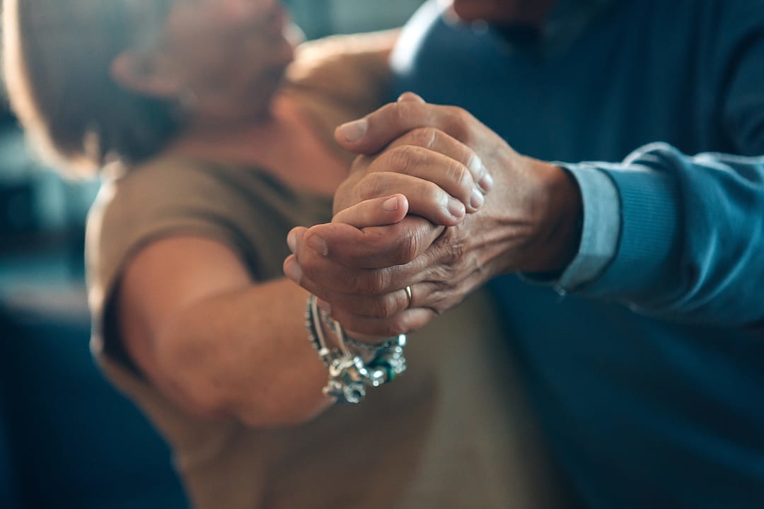 Senior couple holding hands while dancing together indoors.