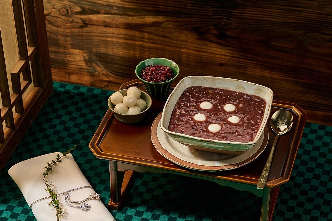 Bowl of Patjuk (Korean red bean porridge) with rice cake balls, served on a wooden table in a traditional Korean setting.