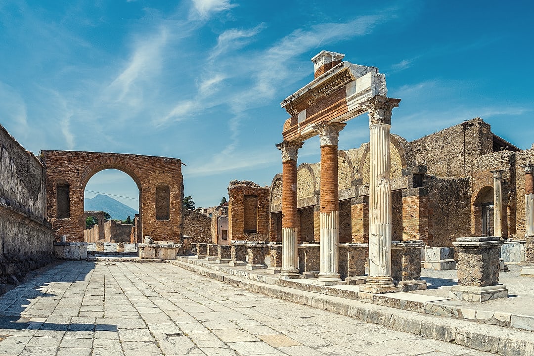 Ancient ruins of the Forum in Pompeii with stone columns and Mount Vesuvius in the background