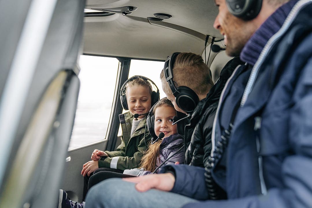 A father and his two young children smile as they look out the window during a helicopter flight.