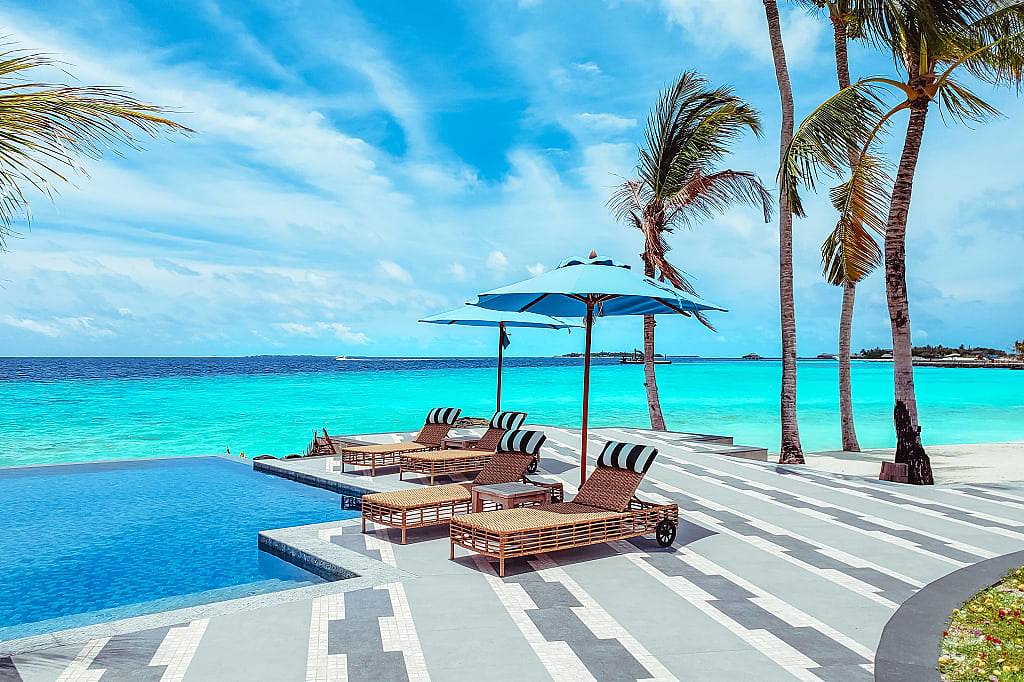 Lounge chairs poolside adjacent to a beach in the Maldives