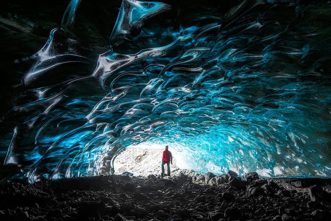 Person standing inside shimmering blue ice cave in Vatnajökull glacier.