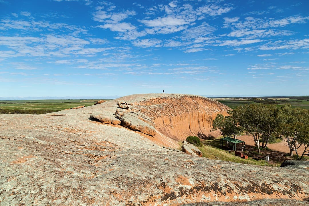 Granite outcrop of Pildappa Rock in South Australia with person standing on summit under blue sky