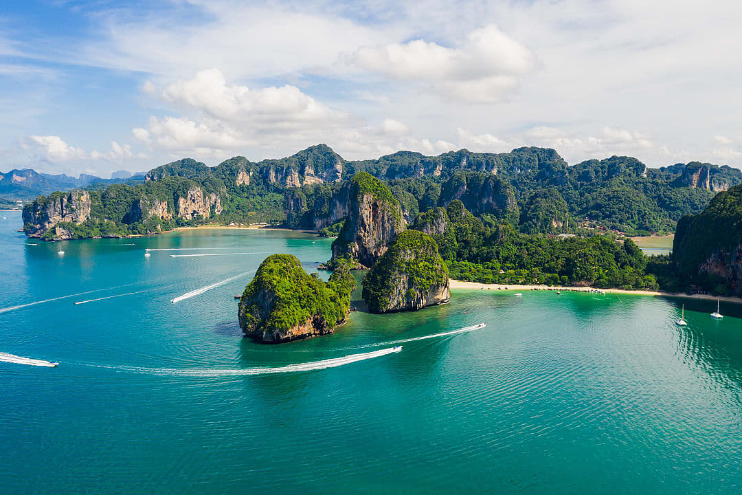 Aerial view of limestone cliffs and turquoise waters off the coast of Krabi, Thailand, with speedboats.