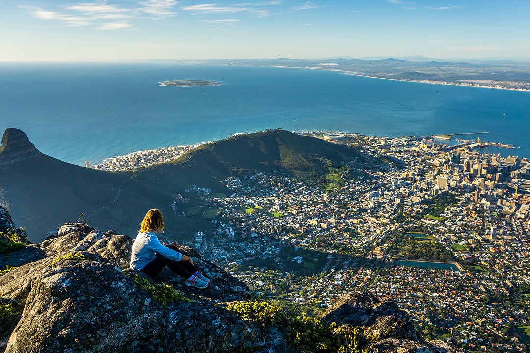 Traveler sitting on Table Mountain, Cape Town, enjoying panoramic views of the city, ocean, and Lion's Head