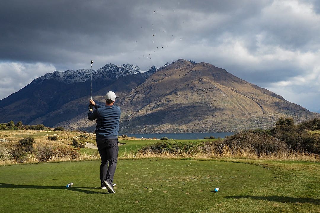 Golfer teeing off at Jack's Point beneath the serrated peaks of The Remarkables