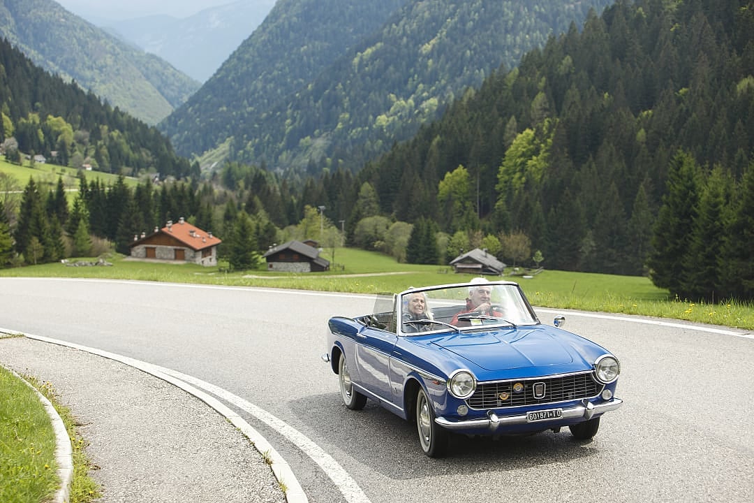 Senior couple driving a classic convertible along a scenic road in Northern Italy