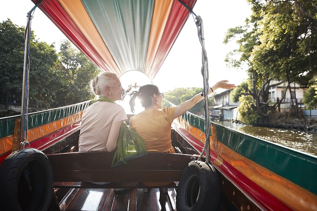 Senior travelers riding a colorful longtail boat through a canal at sunset in Bangkok, Thailand