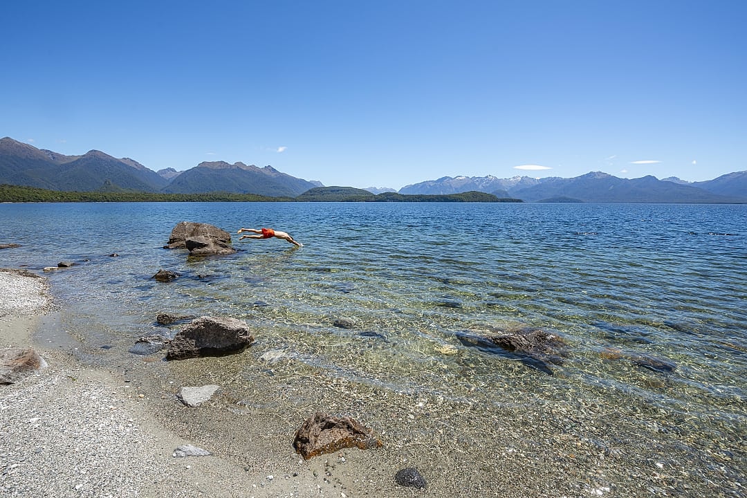 Clear waters, mountain views, swimmer diving in Lake Manapouri.