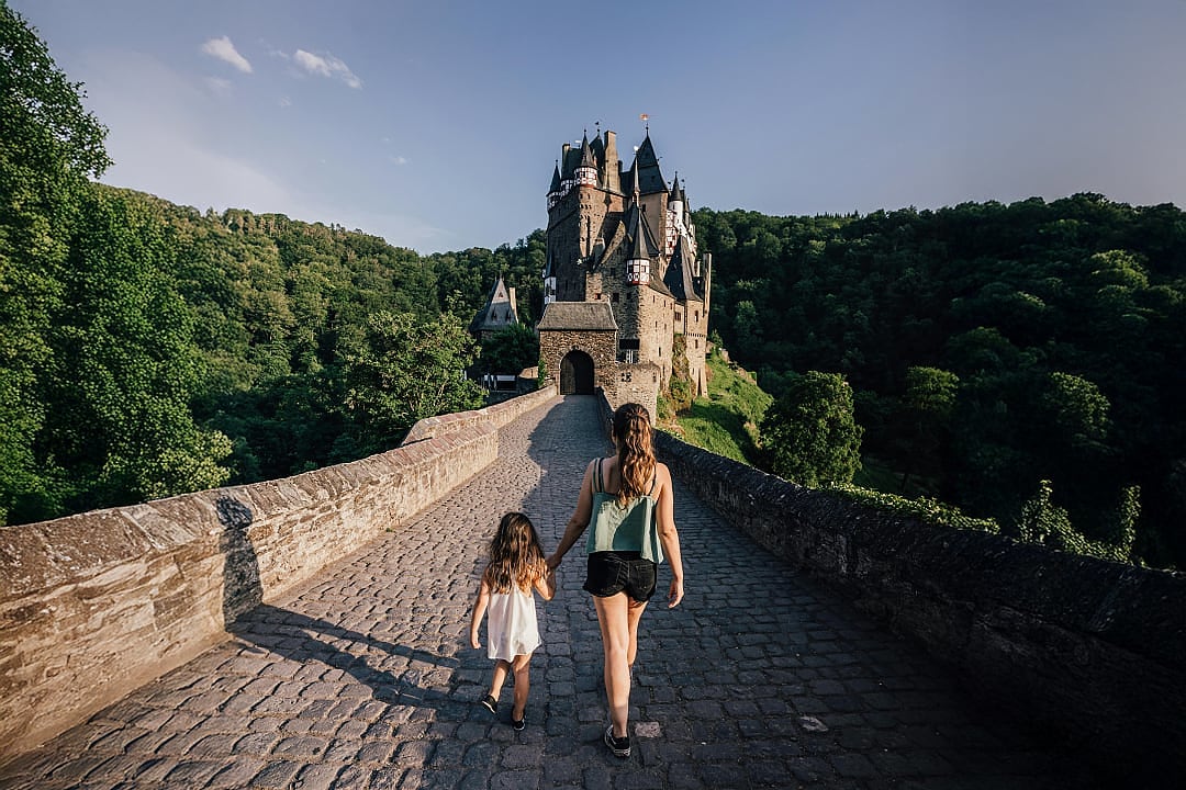 Burg Eltz in Germany with a mother and daughter walking on a cobblestone bridge surrounded by forest
