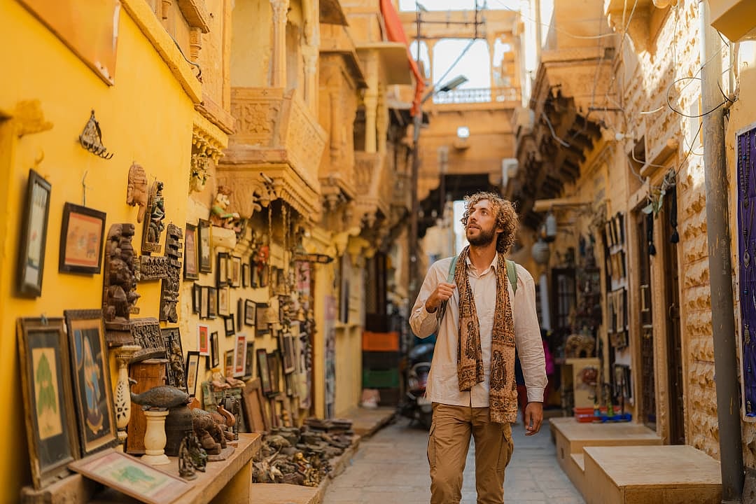 Traveler walking through narrow golden market alley filled with traditional artwork.