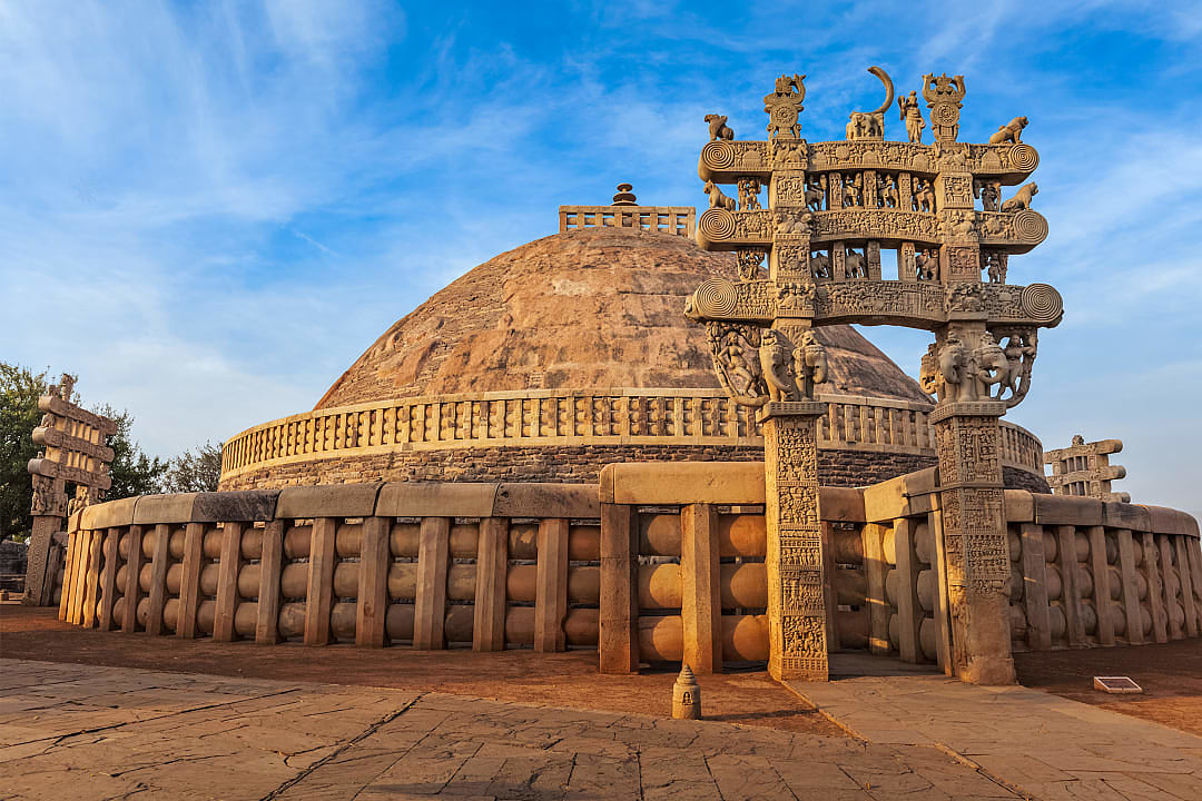 Ancient Great Stupa at Sanchi with ornate gateway under blue sky.