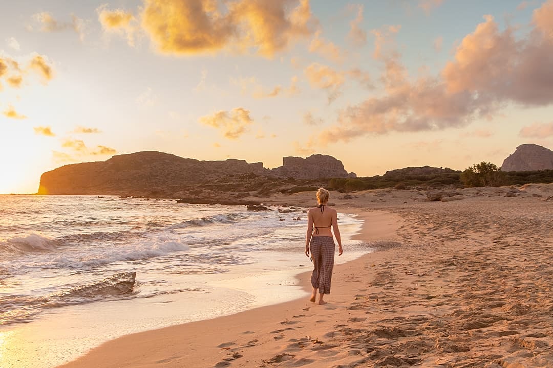 Woman walking on sandy beach at golden hour on Crete, Greece
