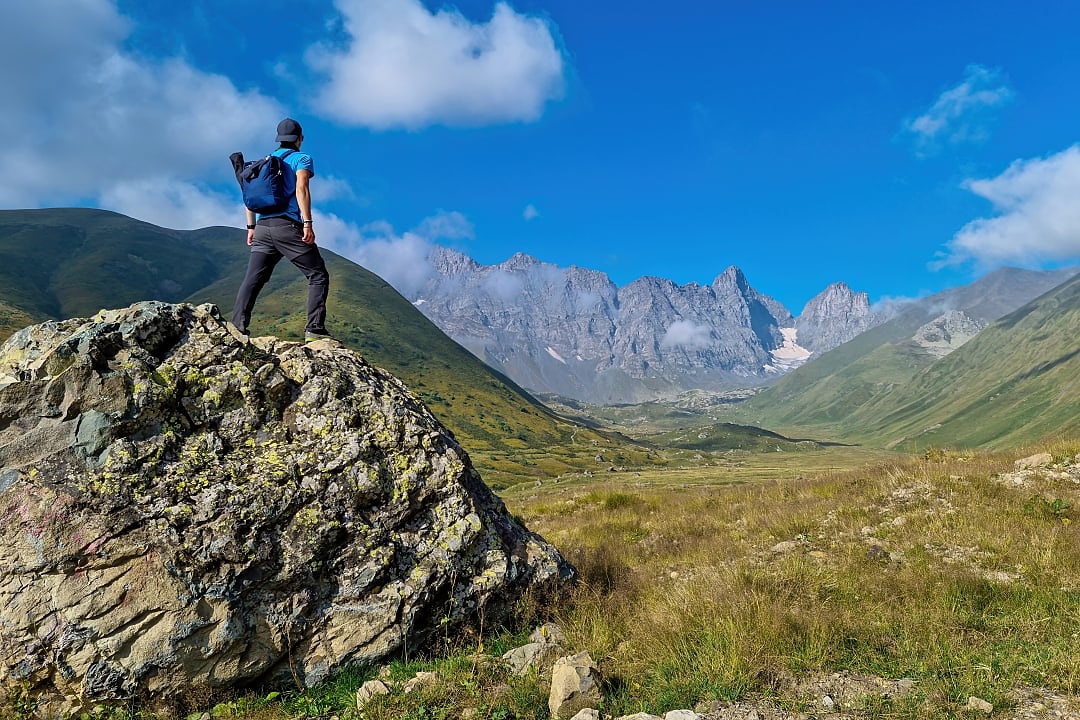 Hiker standing on a rock looking towards Chaukhi Massif in the Georgian Dolomites