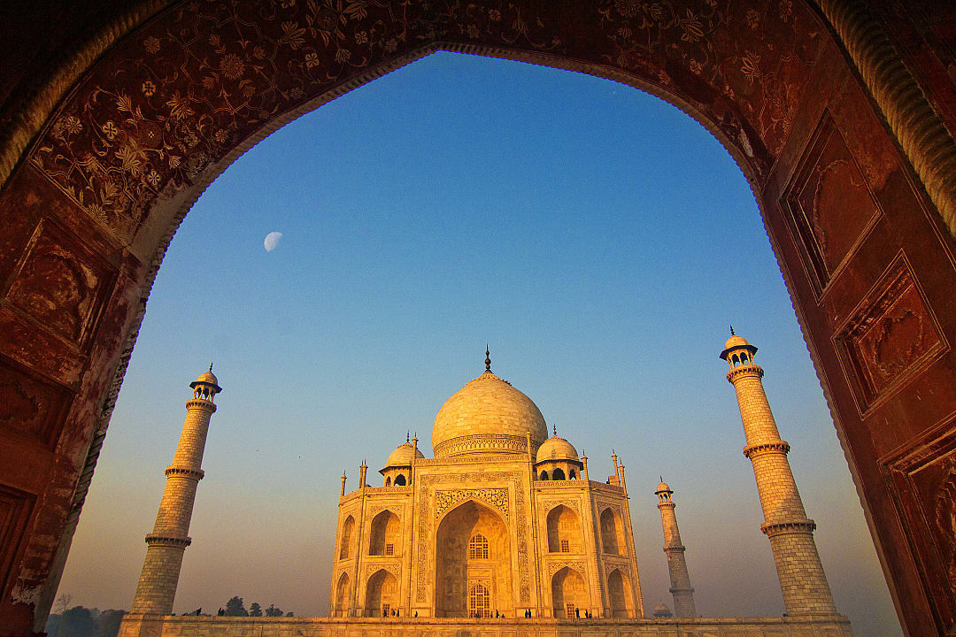 Taj Mahal framed by ornate arch at sunrise.