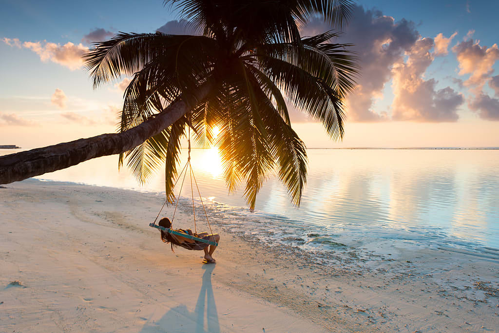 Woman lounging in a hanging chair watching the sunset in the Maldives