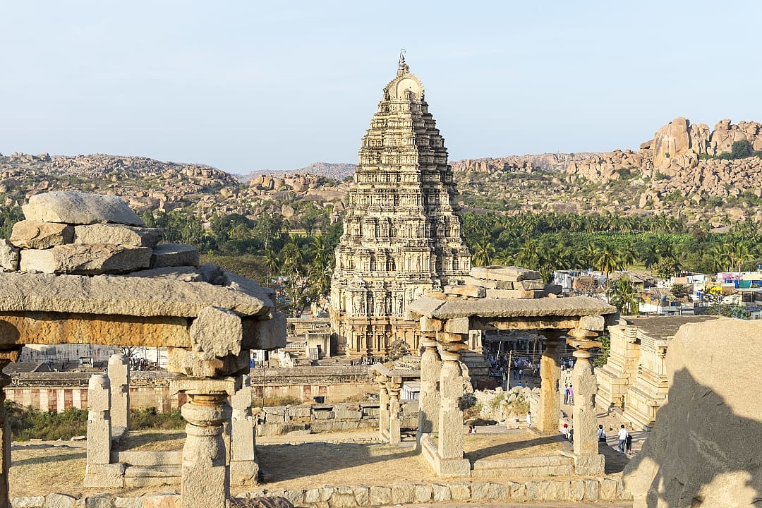 Ancient temple complex with tall stone tower and surrounding ruins in warm light.