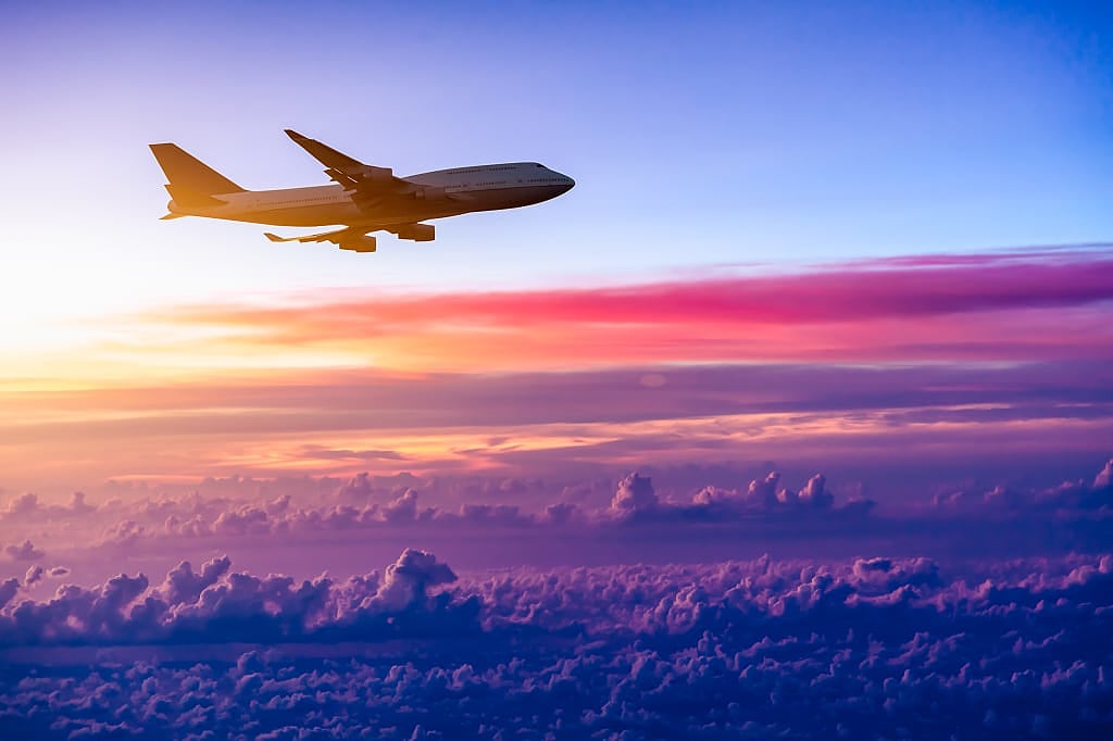 Airplane in flight over clouds during sunset