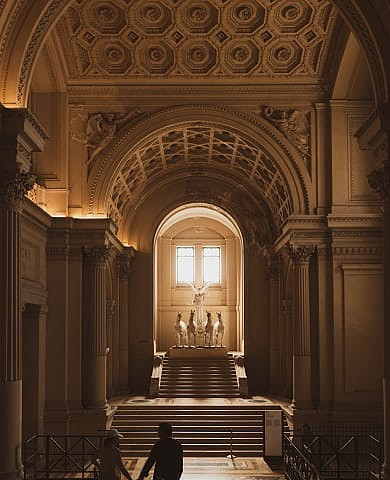 Visitors explore grand museum hall with ornate arches and horse statues.