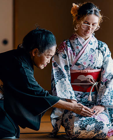 Instructor guides woman dressed in kimono during traditional ceremony.