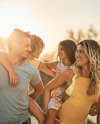 Happy family enjoys playful piggyback rides outdoors at sunset.