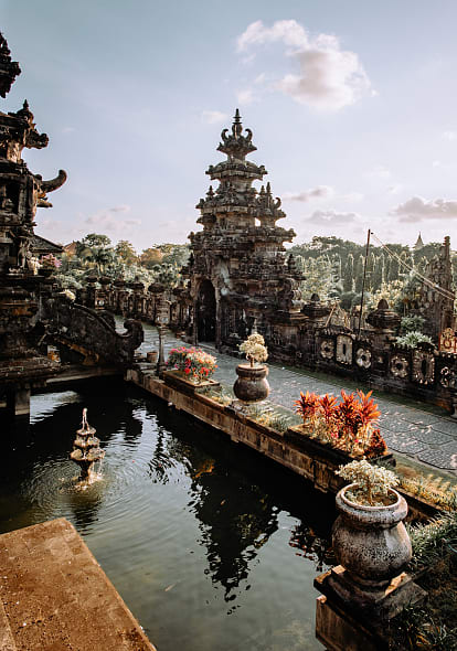 Balinese temple with intricate stone carvings, tropical plants, and reflecting pond under soft daylight