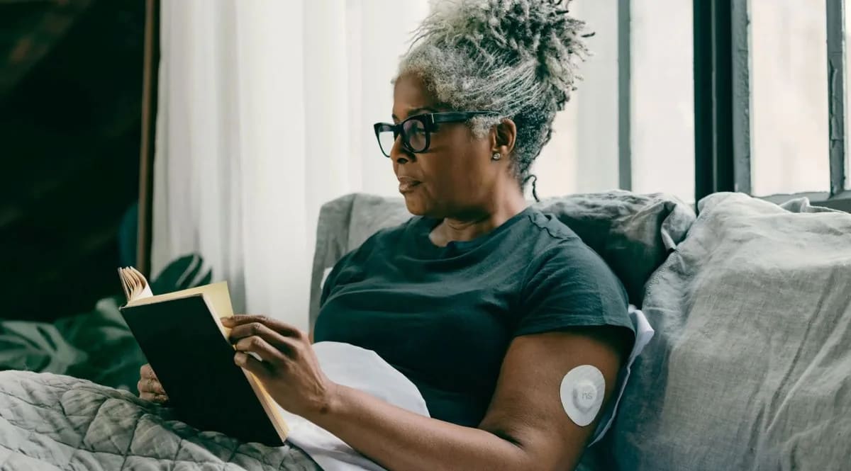 A woman wearing an arm sensor reads a book at home